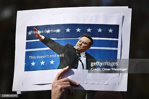 Demonstrator holds a banner depicting a photo of Elon Musk with his armed raised similarly to a "Nazi salute" as people participate in a "Hands Off"...