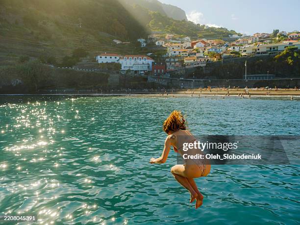 mujer saltando al agua en la playa de seixal durante un viaje experiencial en la isla de madeira, portugal - tomar el sol fotografías e imágenes de stock