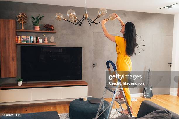 woman changing a light bulb in a cozy room - fitting stockfoto's en -beelden