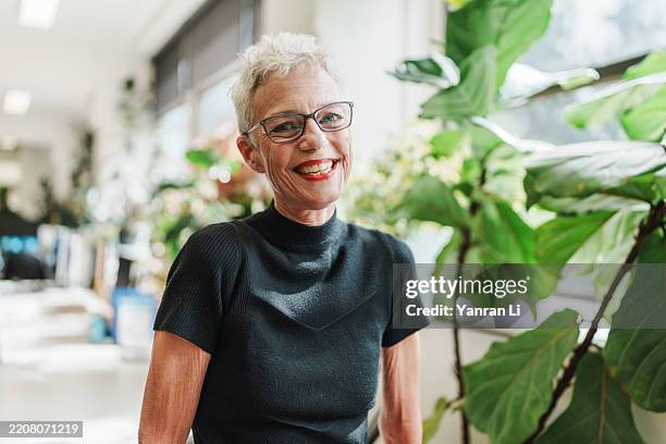 stylish mature woman smiling warmly in a modern vibrant office - werkende bejaarden stockfoto's en -beelden