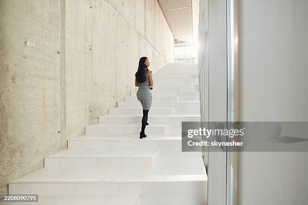 rear view of chinese businesswoman moving up the stairs in a hallway. - steps and staircases stock pictures, royalty-free photos & images