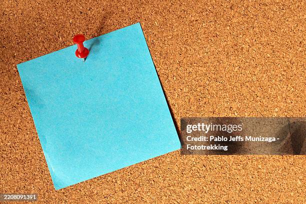 red push pin fastening blank blue sticky note to cork board, highlighting efficient note-taking and organizational workspace strategy - notice board stock pictures, royalty-free photos & images