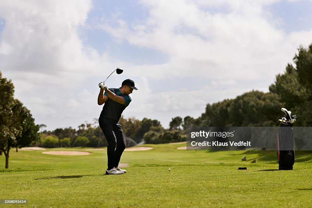 Active male golfer swinging golf club while taking shot