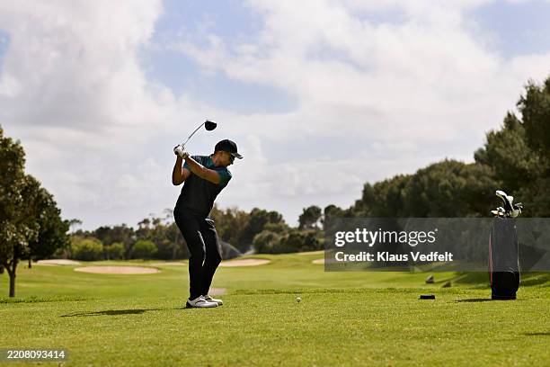 active male golfer swinging golf club while taking shot - campo de golfe imagens e fotografias de stock