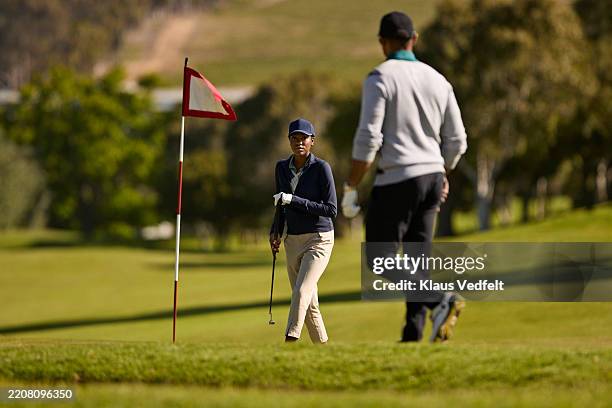 male and female golfers walking towards golf flag - golf flag stock pictures, royalty-free photos & images