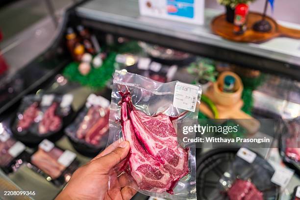 hand holding packaged steak by the meat counter in a grocery store - comida congelada fotografías e imágenes de stock