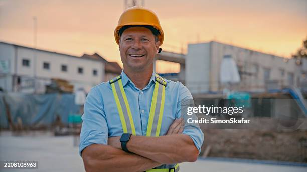 ingeniero masculino seguro de sí mismo sonriendo en el sitio de construcción durante la puesta del sol con equipo de seguridad - scada fotografías e imágenes de stock