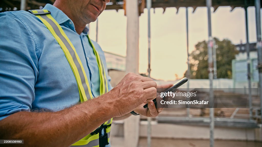 Trabajador de la construcción masculino usando un teléfono inteligente en un sitio de construcción a la luz del día