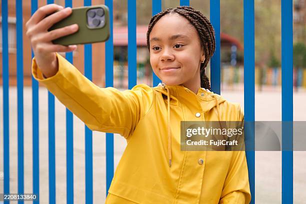 smiling teenager taking a selfie with smartphone wearing a yellow raincoat - mensagem com foto imagens e fotografias de stock