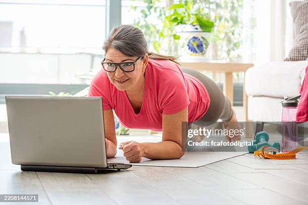 frau, die zu hause übungen macht, während sie sich ein trainingsvideo ansieht. verwenden des laptops während der plank-position - fitnesskurs stock-fotos und bilder