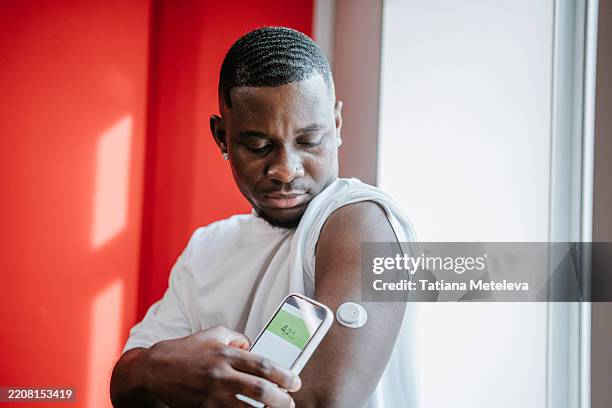 glucose level tracking. serious african american man using continuous monitor on upper arm - glucose stockfoto's en -beelden