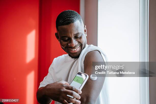 diabetes blood sugar check. smiling interracial man using smart glucose tracker with smartphone app - glucose stockfoto's en -beelden