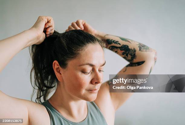 woman tying her hair into a ponytail before workout - queue de cheval photos et images de collection