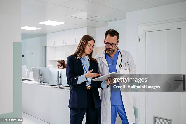 doctor talking with female medical sales respresentative, standing in hospital hallway. - medical sales representative stock pictures, royalty-free photos & images