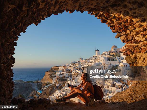 frau mit kamera schaut mit ehrfurcht in oia, santorini - griechische inseln stock-fotos und bilder