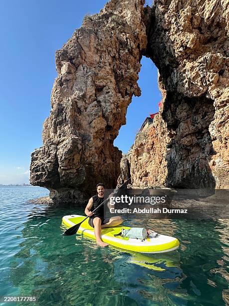 tourist paddling on a stand up paddle board near a beautiful rock formation in antalya - antalya province stock pictures, royalty-free photos & images