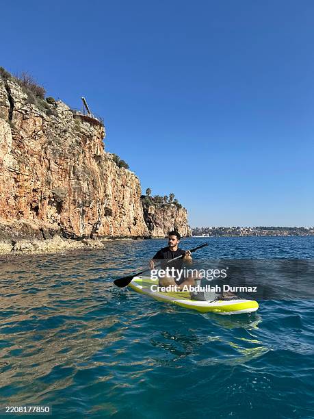 young man paddle boarding in antalya, turkey, with cliffs in the background - antalya province stock pictures, royalty-free photos & images