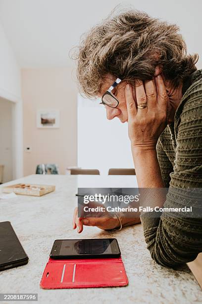 an older woman looks confused as she looks at her smart phone within a pink flip phone cover - staring at screen stock pictures, royalty-free photos & images