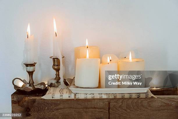 burning candles on wooden shelf. several white candles burning on a rustic wooden shelf with brass holders. - brass stock pictures, royalty-free photos & images