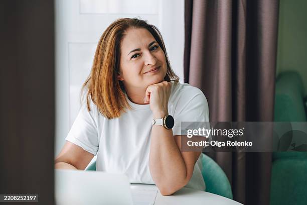 portrait of confident mature woman looking at camera during laptop work - hand on chin stock pictures, royalty-free photos & images