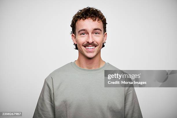 australian young man with curly hair and a mustache smiles against a white background in a casual outfit during a portrait session - solo uomini foto e immagini stock