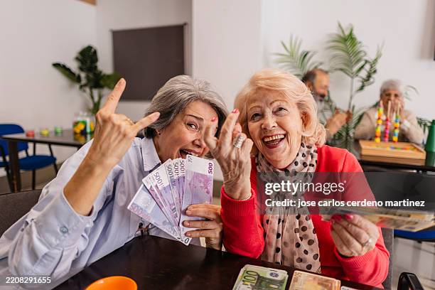 two senior women holding euro banknotes and making rock and roll hand gestures - todas as unidades monetárias europeias imagens e fotografias de stock