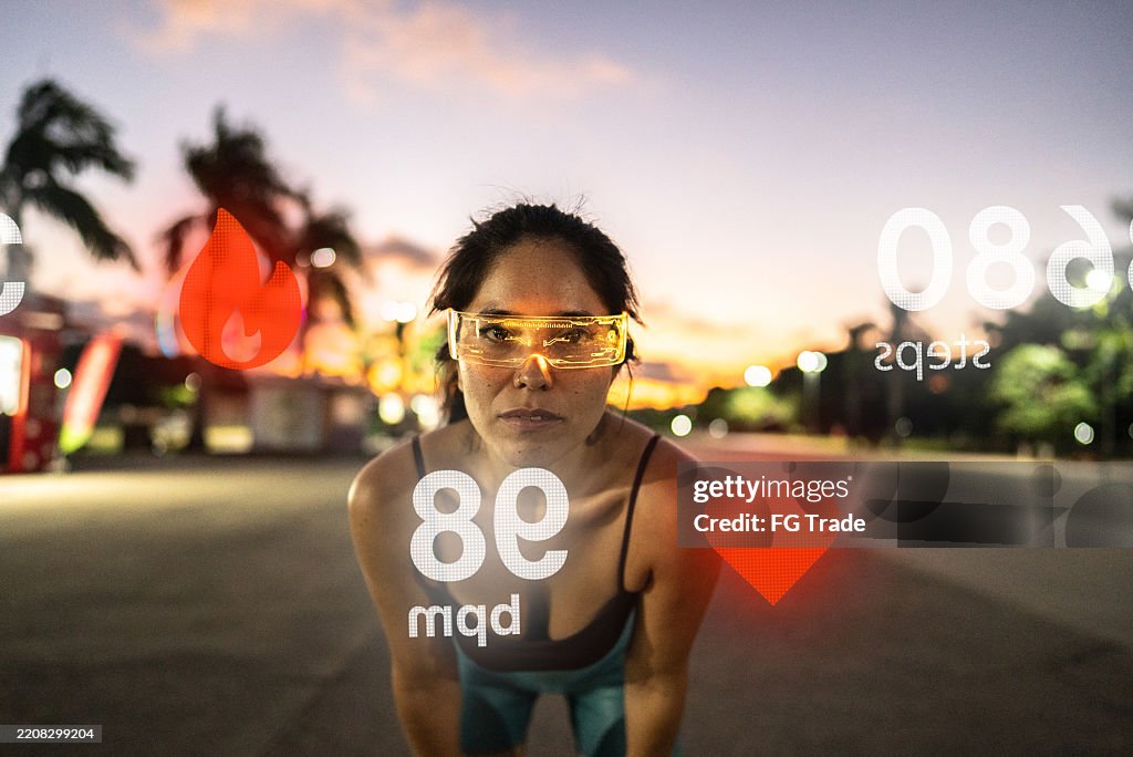 Portrait of a young adult woman with futuristic glasses analyzing data while exercising outdoors