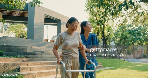 una joven enfermera asiática ayuda a una anciana con un andador a disfrutar del apoyo y la vida activa en el parque. concepto de cuidado de la salud al aire libre. - medicare fotografías e imágenes de stock