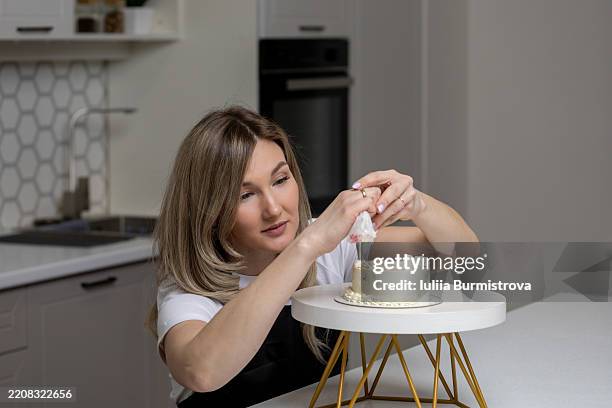 young woman decorating a cake with frosting in a modern kitchen - decorating a cake stock pictures, royalty-free photos & images