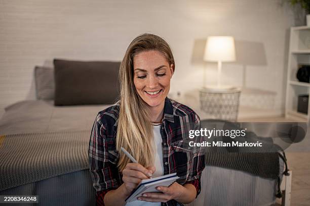 smiling woman writing on notepad in bedroom at home - minimal art stockfoto's en -beelden