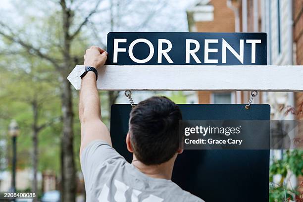man puts up a for rent sign in front of house - huurhuis stockfoto's en -beelden