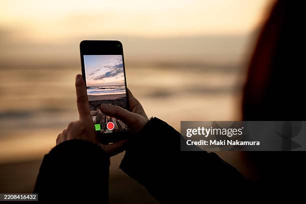 the woman's finger rests on the iphone capture button, capturing the fleeting natural beauty of the morning ocean. - mit mobilgerät aufgenommen stock-fotos und bilder