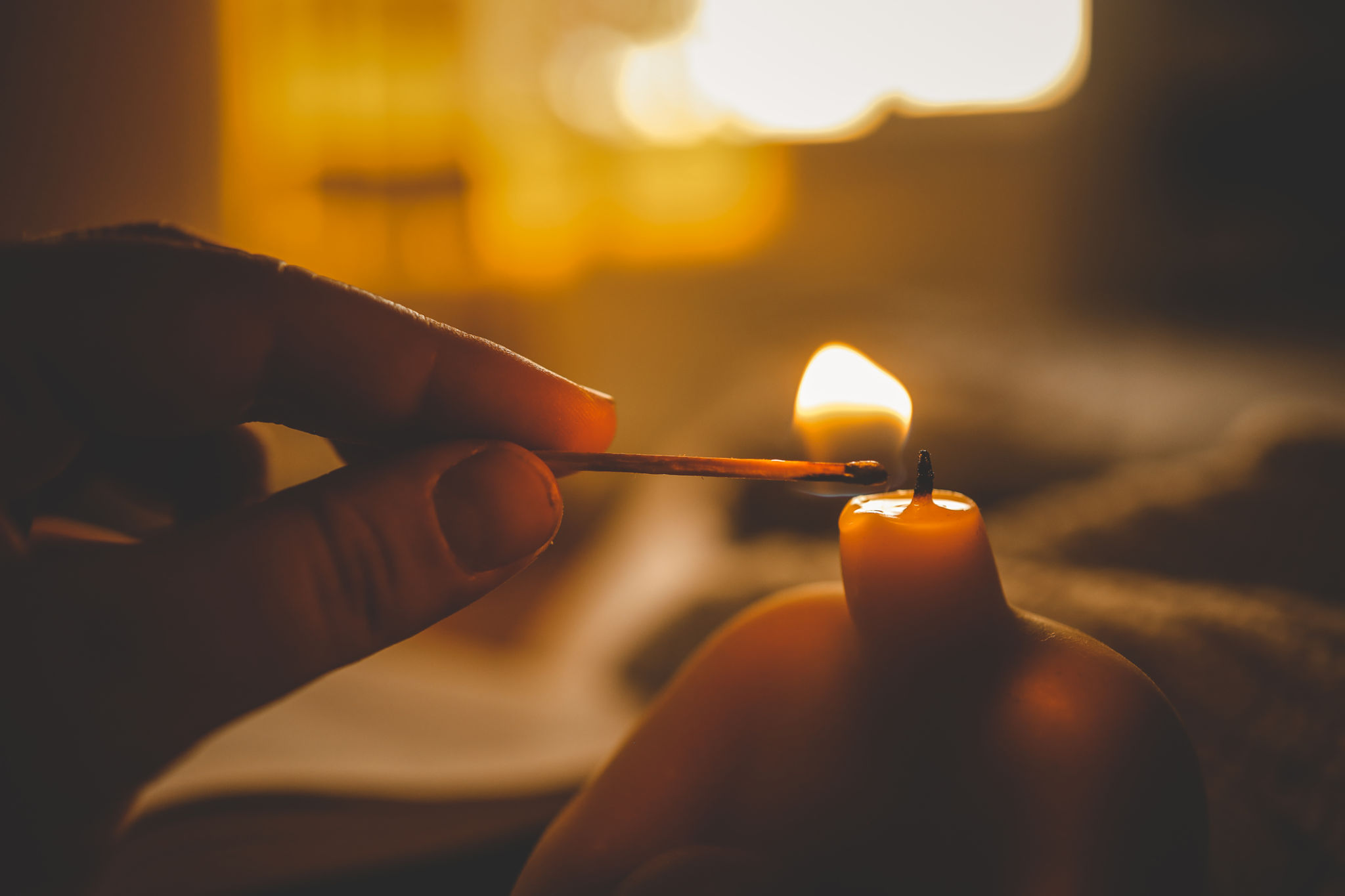Close-up of a hand lighting a sculptural candle with a match in warm ambient light Close-up of a hand lighting a sculptural candle with a match in warm ambient light