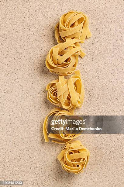 raw uncooked fettuccine pasta nests on beige background - carbohidrato fotografías e imágenes de stock