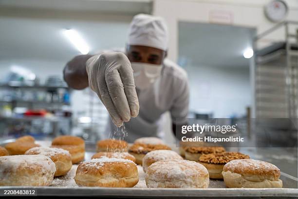 panadero espolvoreando azúcar glas sobre las rosquillas mientras trabaja en la panadería - azúcar en polvo fotografías e imágenes de stock