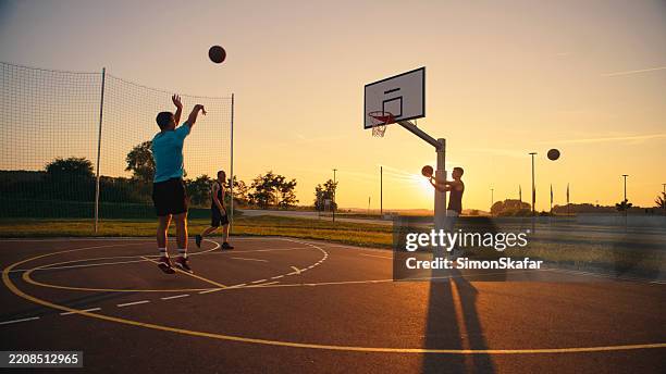 friends playing basketball at sunset - mens basketball stock pictures, royalty-free photos & images
