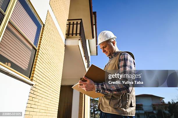 building inspector examining documents outside residential building - kwaliteitscontroleur stockfoto's en -beelden