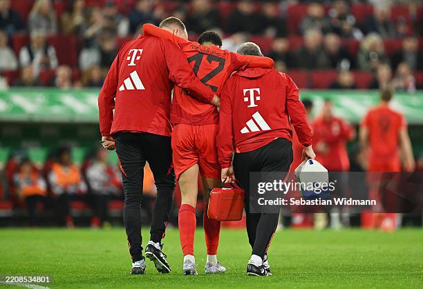 Jamal Musiala of Bayern Munich is helped off the pitch to receive medical treatment during the Bundesliga match between FC Augsburg and FC Bayern...