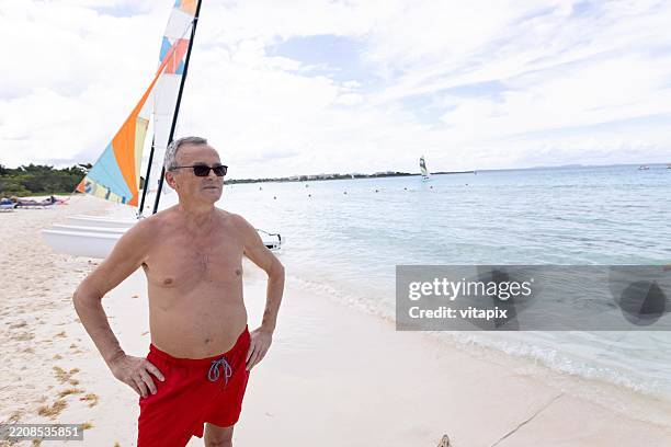 man in red swim trunks relaxing on a tropical beach by the ocean - swimming trunks stock pictures, royalty-free photos & images