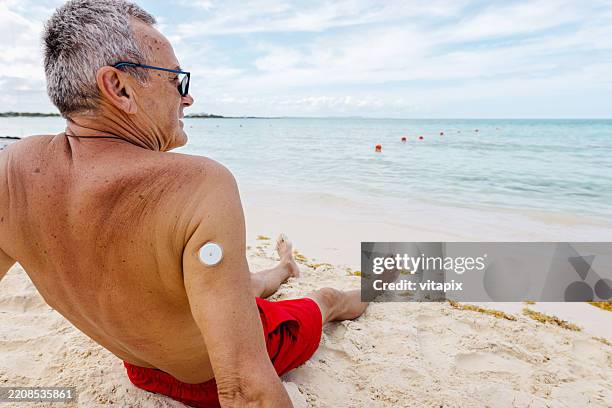 man relaxing on beach with health device on shoulder - glucose stockfoto's en -beelden