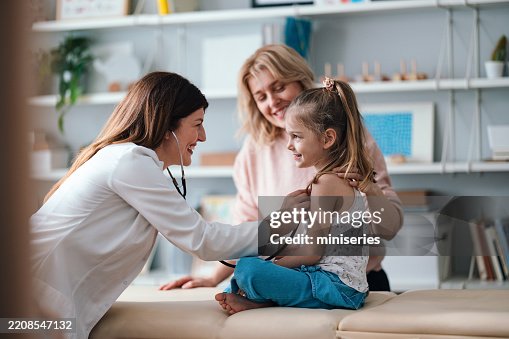 Smiling Pediatrician Examining a Cheerful Young Girl During a Checkup Smiling Pediatrician Examining a Cheerful Young Girl During a Checkup