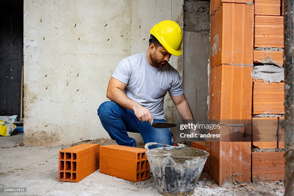 Trabajador de la construcción construyendo un muro de ladrillos en una obra de construcción