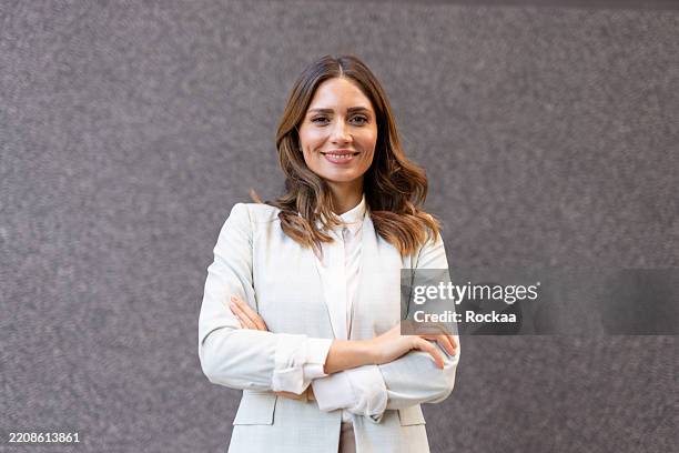 femme d’affaires confiante souriant avec les bras croisés devant le mur gris - costume complet photos et images de collection