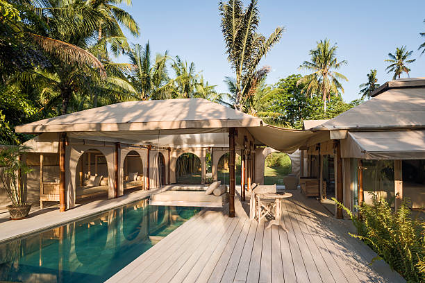 tented villa at eco friendly luxury glamping resort with open side panels showing open plan interior, situated amongst lush tropical foliage outdoors, with salt water swimming pool - luxury resorts stock pictures, royalty-free photos & images