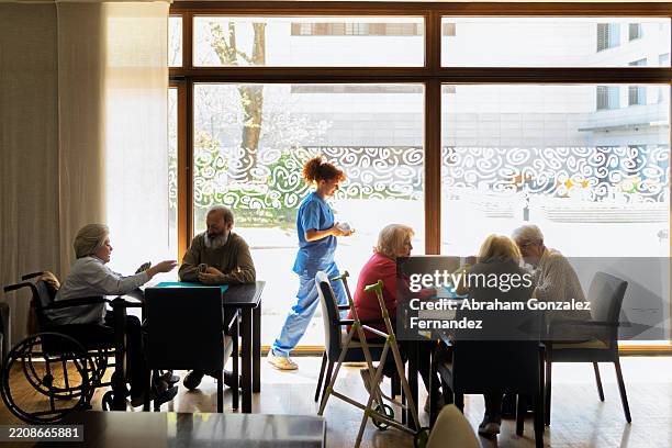 nurse assisting elderly patients in a retirement home common room, providing care and support for their daily needs - rusthuis stockfoto's en -beelden