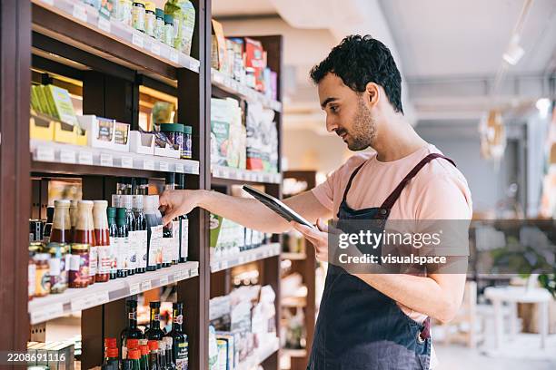 un employé de magasin utilise une tablette numérique pour vérifier les stocks, en examinant le stock de produits sur les étagères du magasin - employé de magasin photos et images de collection