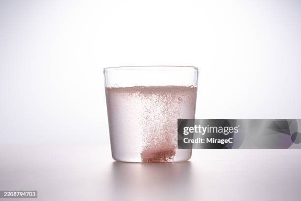 pink effervescent tablet dissolving in a glass of water - disolver fotografías e imágenes de stock