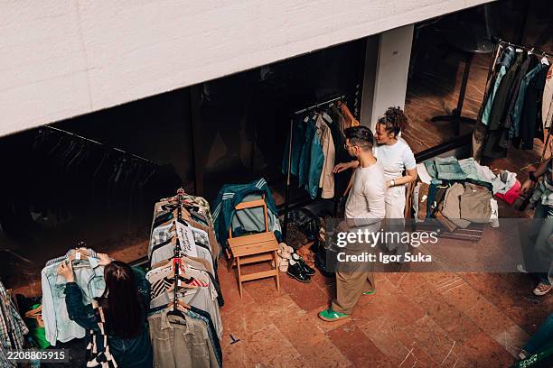 kunden stöbern an einem flohmarktstand nach kleidung, der secondhand-kleidung verkauft - flohmarkt stock-fotos und bilder