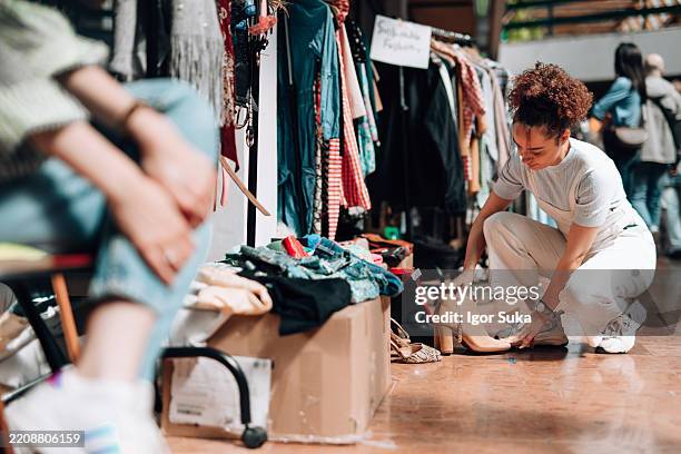 woman choosing second hand boots in sustainable fashion market - circulaire economie stockfoto's en -beelden