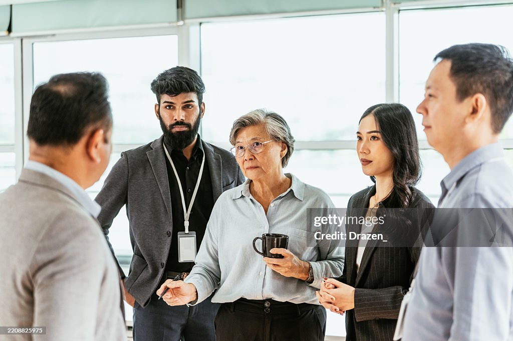 Diverse business people talking to senior female CEO during coffee break on business seminar